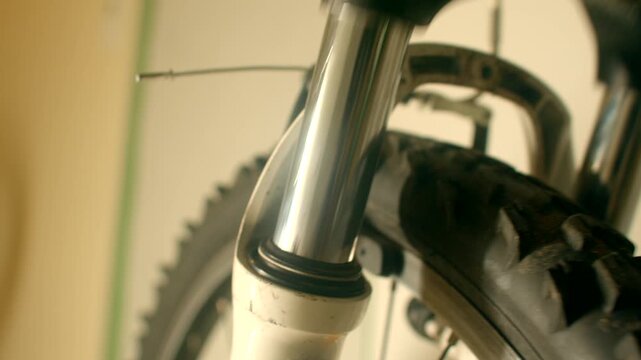 Closeup fork suspension stanchion travel mudsplattered tire, slow compression and rebound, subtle squeak as shock absorbs impact, objects make sound during ride inspection