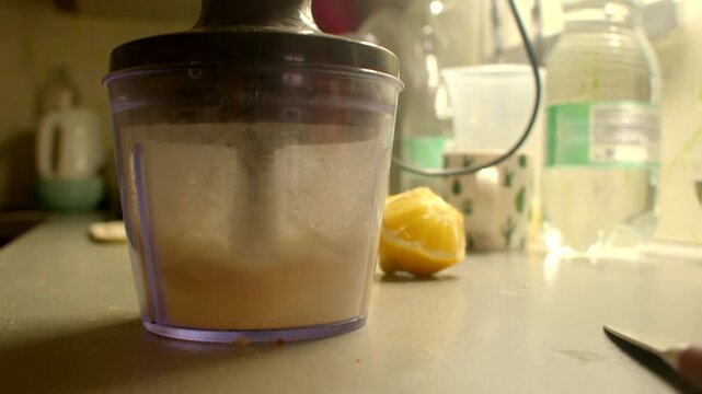 Counter chopper making chopping sound closeup of plastic container processing butter next to knife and bottle warm yellow lighting gritty kitchen atmosphere motor vibration