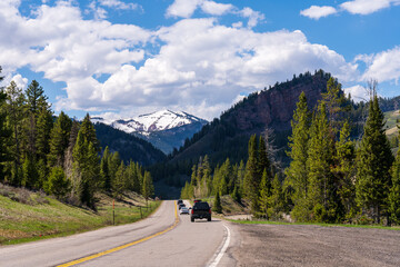 Naklejka premium Open highway road trip through the majestic Rocky Mountains of the American West under a blue sky.