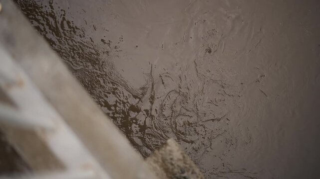 Urban muddy water with reflections. Rainsoaked urban puddle reflecting dull sky above structure. Glistening muddy surface of rainfilled puddle with ripples and city reflections across water