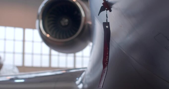 Red remove before flight tag near engine, closeup of safety ribbon and lanyard against turbine background suggesting ground crew preflight checklist and regulatory inspection