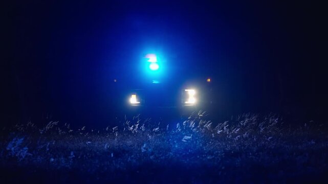 Flashing police lights in distance on dark road at night with headlights and strong glow creating cinematic emergency tension and atmospheric scene