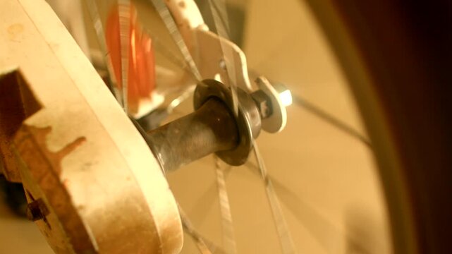 Spinning bicycle reflector hits spokes, warm sepia closeup of metal hub and wooden fork, orange reflector blur shows rotation, audible clicks and clacks as objects make sound,