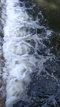 A small river dam with fast-flowing water below is used for irrigation in a rural area
