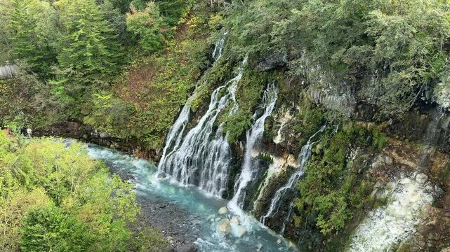 Shirahige Waterfall with deep cobalt blue hue, Waterfall of Shirahige and Tokachidake Mountain Range in Biei-cho, Hokkaido Japan in early fall or autumn season. famous tourist destination in Biei