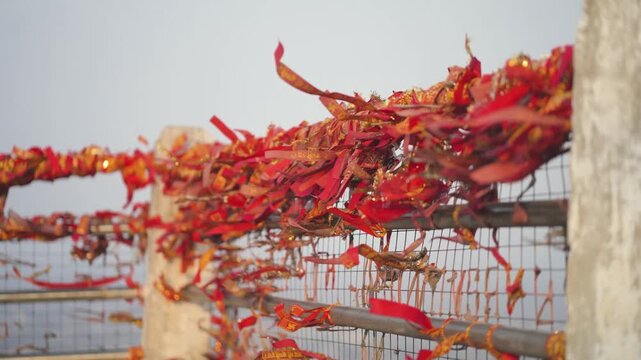 Sacred red threads on temple railing, religious ribbons tied at shrine, faith threads fluttering in wind, devotional ties at holy place stock video.