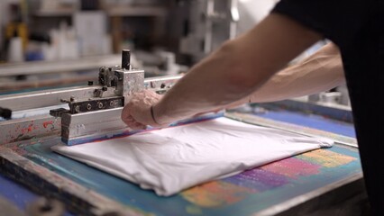 Fototapeta premium Close-up of worker performing screen printing process on a white T-shirt in a professional studio