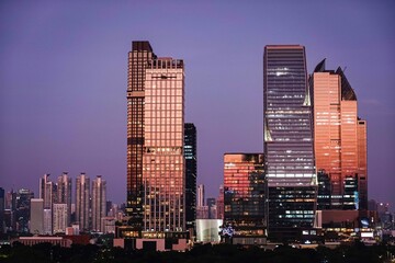 Naklejka premium Beautiful Bangkok skyline during sunset purple sky with modern glass skyscrapers reflecting warm golden light. Urban cityscapes and travel destinations in Bangkok,Thailand Southeast Asia.