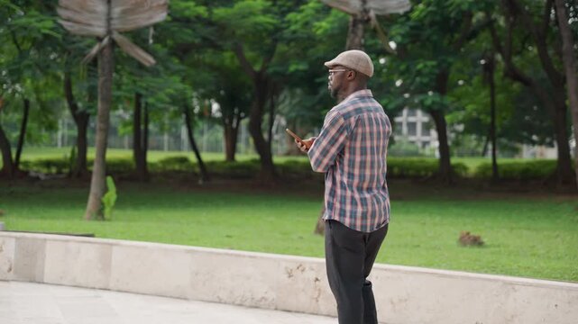 Individual walking with mobile phone. Man leisurely strolling while viewing his mobile screen. Individual casually moving along low stone barrier while concentrating on mobile device screen
