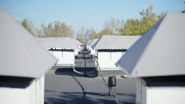 Building roof features dark dense non-slip material covering. Rows of small ventilation dormers stay connected by long electrical wires