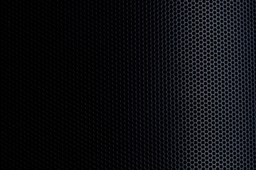 Naklejka premium A high-resolution, close-up shot of a black metallic perforated mesh surface. The image features a dramatic lighting gradient from deep shadows on the left to highlighted circular patterns.