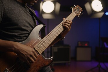 Naklejka premium A person plays an electric bass guitar with intense focus in a relaxed studio setting surrounded by professional lighting equipment.