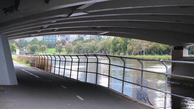 Shared cycling and walking path under Yarra River bridge with green parkland, city skyline in the background, Melbourne Australia.&nbsp;Riverside trail network and active transport infrastructure