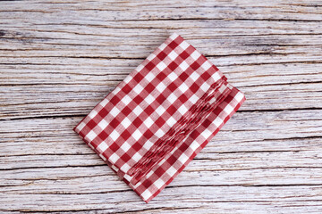 Obraz premium Red and white checkered cloth napkin rests on wood. Folds show soft texture and gentle creases. Rustic background adds charm and nostalgia. Ideal for kitchens, cafes, or picnic scenes