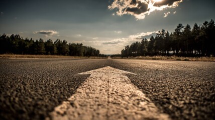 Obraz premium Forward Arrow Painted on Asphalt Road Leading Through Forest Towards Horizon at Sunset