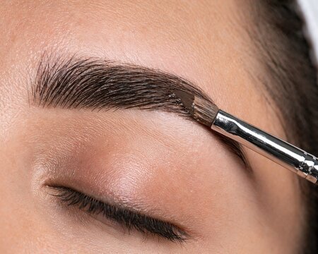 Woman applying eyebrow makeup with brush closeup in beauty salon  