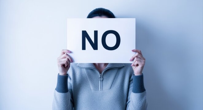Person Holding Sign with Large 'NO' Text Blocking Face Against Textured Wall