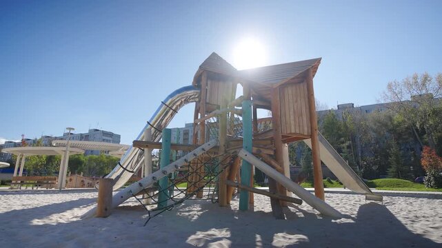 Playground with carefully shaped elements stands in city filled with golden light. Beautifully crafted playground with timber structures