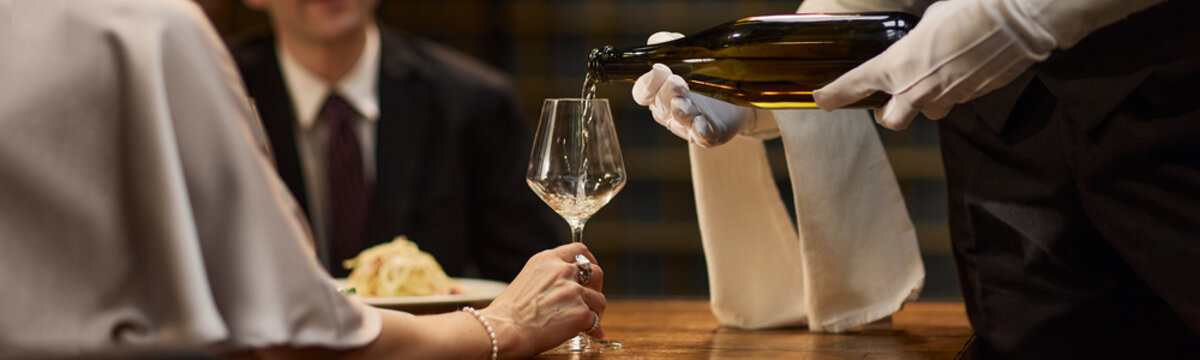 Header of waiter pouring sparkling wine for middle aged couple during restaurant dining, representing luxury hospitality. Suitable for fine dining marketing, service promotion, close up