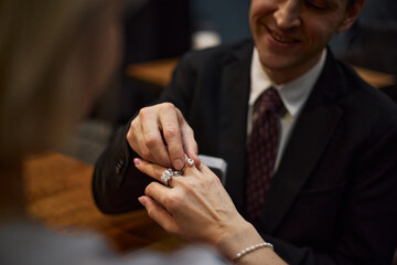 Caucasian adult man placing engagement ring on woman hand during proposal, symbolizing commitment...