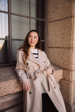 Stylish woman in trench coat standing by window in urban setting