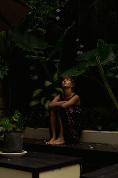 Woman sitting on steps looking up in dark tropical garden, Bali