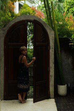 Woman opening arched wooden door looking over shoulder, Bali