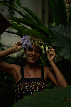 Smiling woman holding blue flowers over head in tropical garden, Bali