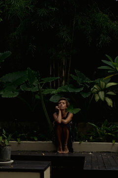 Woman sitting on steps with head on hands eyes closed, Bali