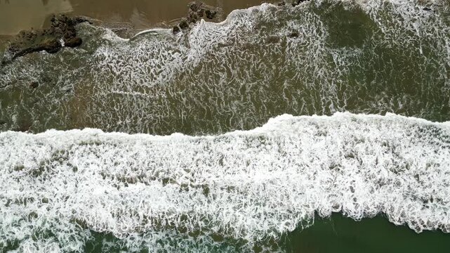 Aerial drone flight following rolling waves towards the shore of Mancora beach, Peru