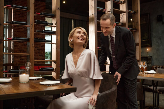 Caucasian couple dining in restaurant, man pulling chair for woman and sharing romantic date moment, representing hospitality and relationship marketing for luxury dining promotions