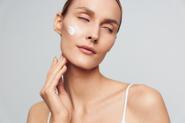 Woman skincare beauty portrait with cotton pad and moisturizer, self care for healthy skin in a spa style close up, calm female face, grey studio background soft light care