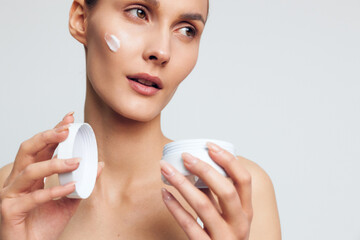 Young woman performs skincare on face using cotton pads, applying moisturizer and cream for beauty, hygiene routine and gentle treatment in a bright clean studio