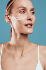 Woman skincare face cream close up blue background self care wellness beauty applying moisturizer, calm smile, spa routine, soft studio lighting, healthy skin hydration