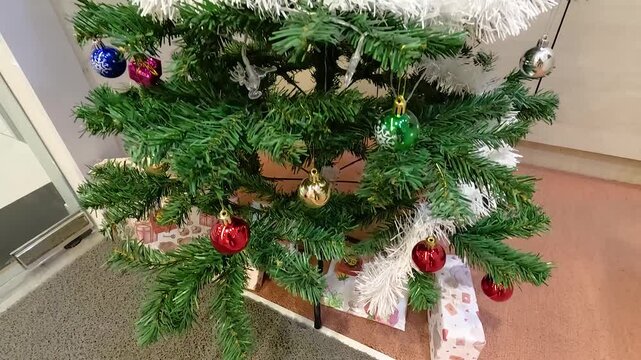 Close up of a decorated Christmas tree with ornaments and presents underneath, slow zoom out reveals full tree.