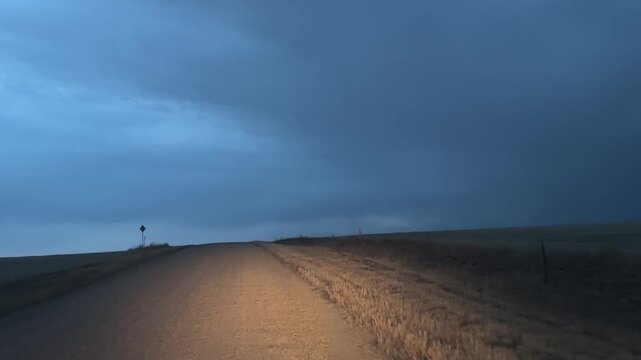 POV driving on gravel road at night through rural landscape with dark sky and limited visibility