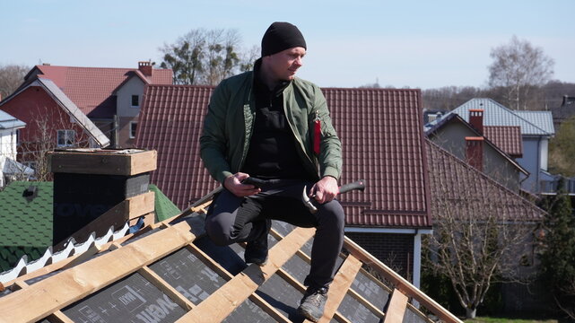Roofing work. A dismantled roof, work to replace the tiles. A man inspects the work being done to install new tiles on the roof. A foreman on the roof looks at the progress.