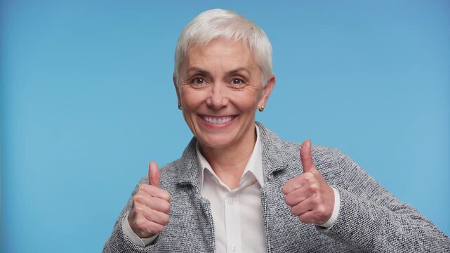 Smiling senior woman showing thumbs up on blue