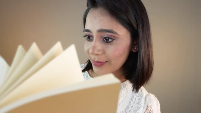 Close up of happy young Asian woman flipping a book pages, isolated against grey studio background.