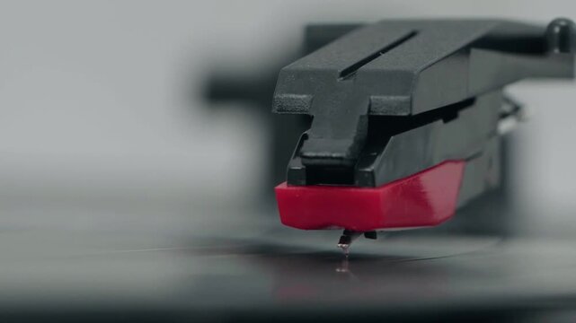 Red stylus contacts vinyl gently. Black tonearm holds steady above record. Soft focus blurs background slightly. Music lover's quiet moment captured. Ideal for retro audio, vintage vibes
