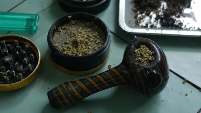 Glass Hand Pipe with Colorful Striped Design and Herb Grinder on Teal Table for Cannabis Lifestyle