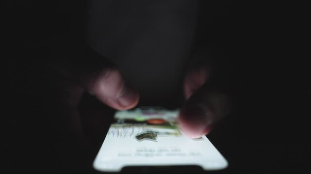 Man swiping on the screen while using smartphone in the dark. Slow motion