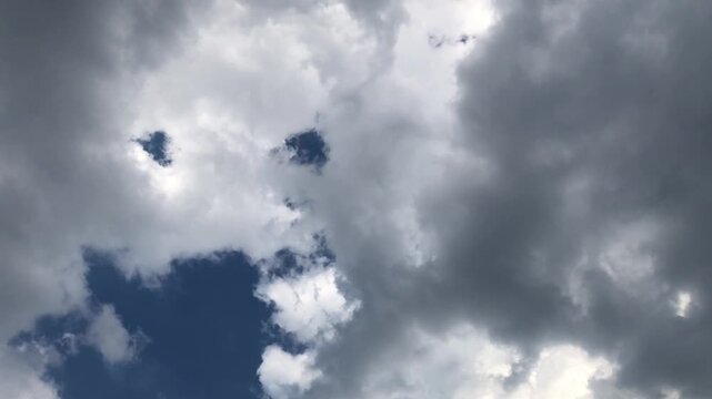 A cloudy sky with two openings resembling eyes and a mouth, creating a face-like appearance against a backdrop of dark storm clouds.