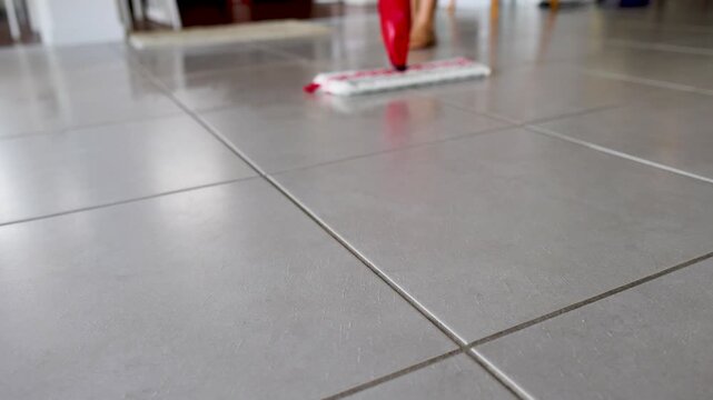 A close up view of a cleaning mop in motion cleaning a tiled floor in a residential house.