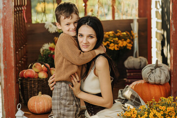 Fototapeta premium Gentle hugs of a mother and a young son on the steps of a house surrounded by autumn decor