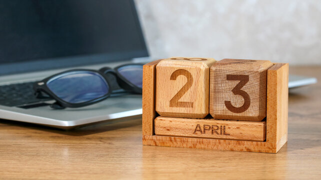 Wooden calendar blocks showing April 23 on a desk with laptop and glasses, concept of planning and time management