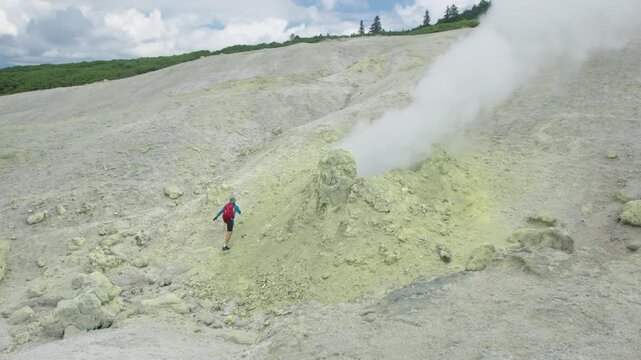 Person approaches the actively smoking fumarole on the wild volcanic area of the volcano of Mendeleev on Kunashir Island in Russia