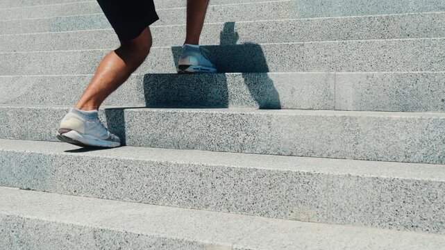 Young man exercising outside. Back side view of guy's legs doing one leg squat exercises stepping forward and skipping one step. Exercising on street under the sun.