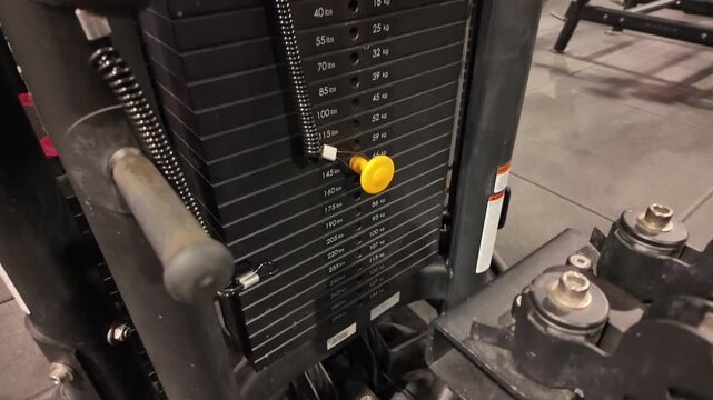 close up of black weight stack machine in gym with yellow pin selector and metal guides showing industrial fitness equipment detail