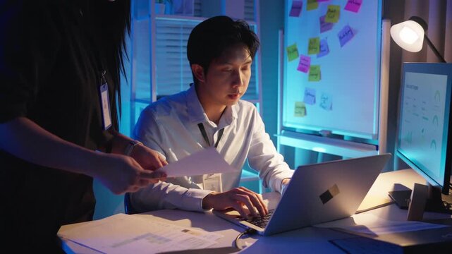 Asian business team discussing report document together while working late at night in modern dark office